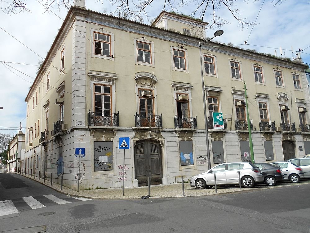 Old abandoned European building with boarded windows and graffiti on walls at street corner with parked cars