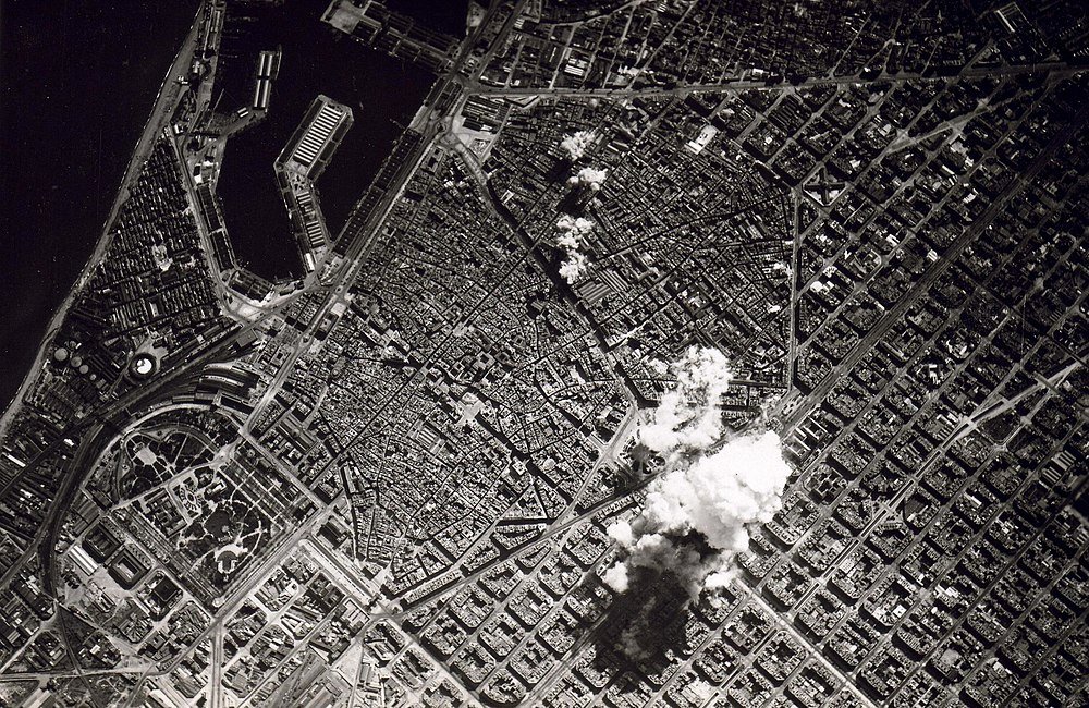 Aerial view of city with explosion and smoke Aerial black and white photo of a city with dense buildings and smoke rising from an explosion site