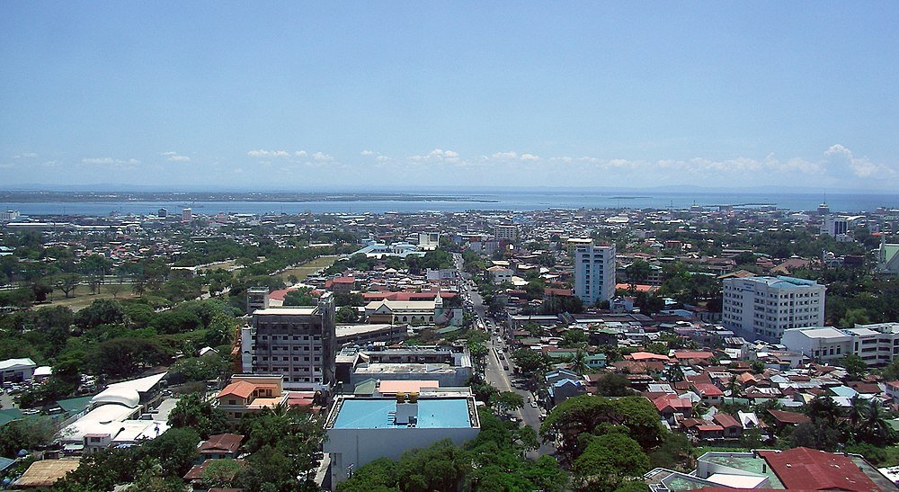 Aerial coastal cityscape with buildings and ocean view Aerial view of a coastal city with buildings, greenery, and a clear blue sky near the ocean on a sunny day