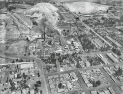 Aerial view of industrial town with factories and homes Aerial black and white photo of an industrial town with factories, residential houses, and surrounding hills.