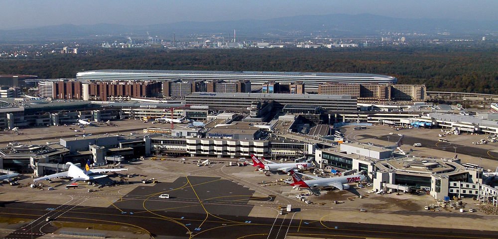 Aerial view of a busy international airport with multiple airplanes parked at gates and terminal buildings visible