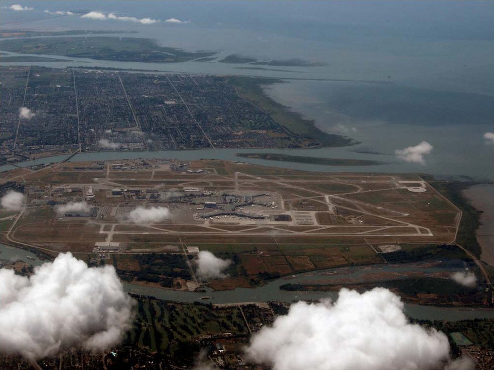 Aerial view of island airport with runways and terminals Aerial view of a large airport on an island surrounded by water and urban areas with runways and terminals visible