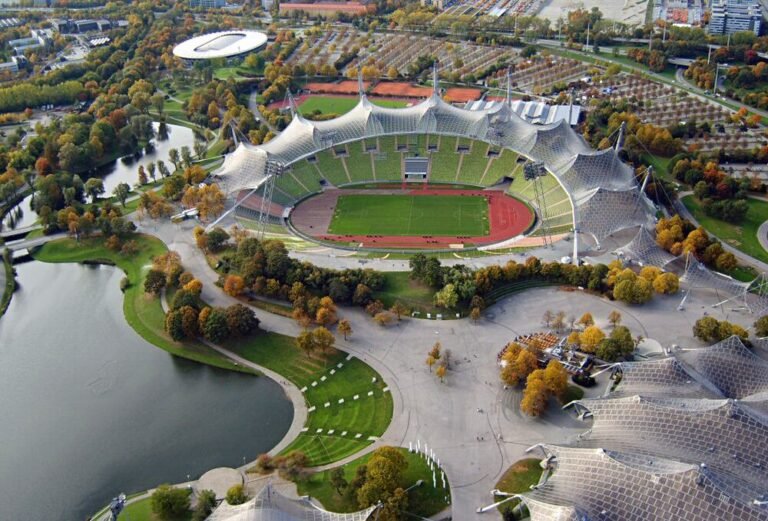 Aerial view of Munich's Olympic Stadium with its iconic sweeping tent roof, set among the lakes and trees of the Olympiapark