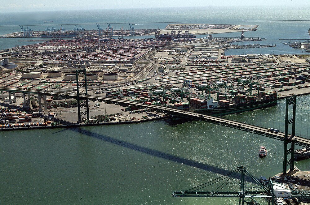 Aerial view of busy shipping port and suspension bridge Aerial view of a busy shipping port with container cranes, cargo ships, and a large suspension bridge over water