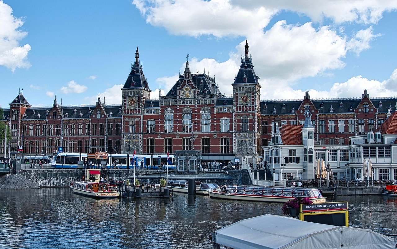 Historic Amsterdam Central Station with canal boats and tram under a bright blue sky in the Netherlands