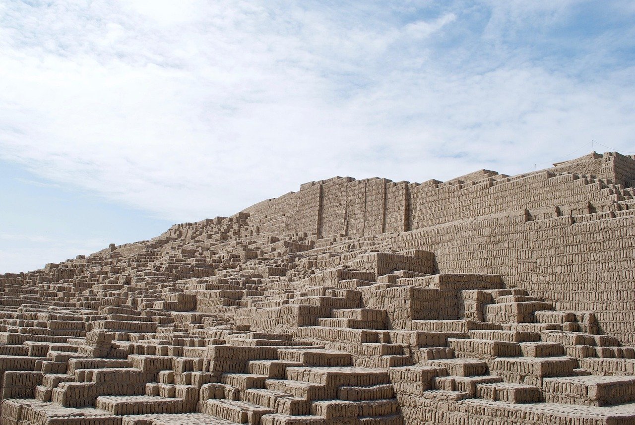 Ancient adobe brick pyramid ruins under a partly cloudy sky, showcasing stepped architecture and historical significance