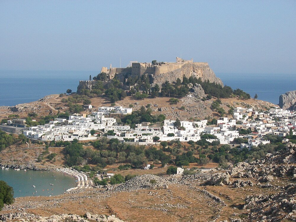 Ancient fortress and coastal town landscape Ancient fortress on a rocky hill overlooking a coastal town with white buildings and a blue sea background