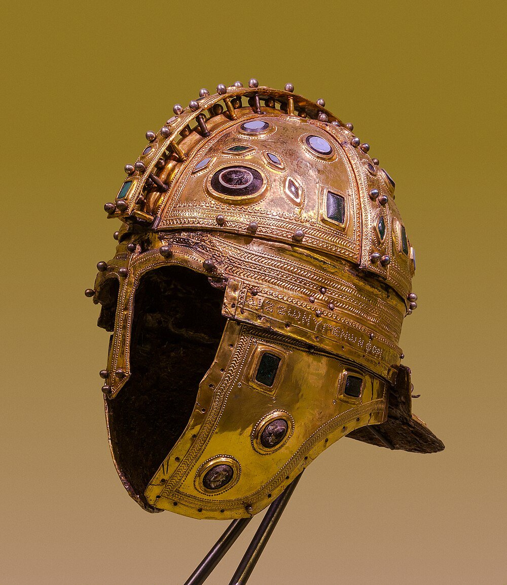 Ancient ornate gold helmet with embedded gemstones and intricate detailing from historical armor collection