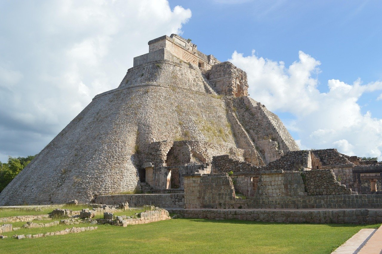 Ancient Mayan pyramid with stone steps and ruins under a blue sky with clouds, showcasing historic architecture