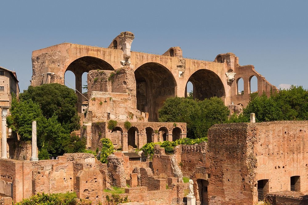Ancient Roman ruins with large arches and brick structures surrounded by greenery under clear blue sky