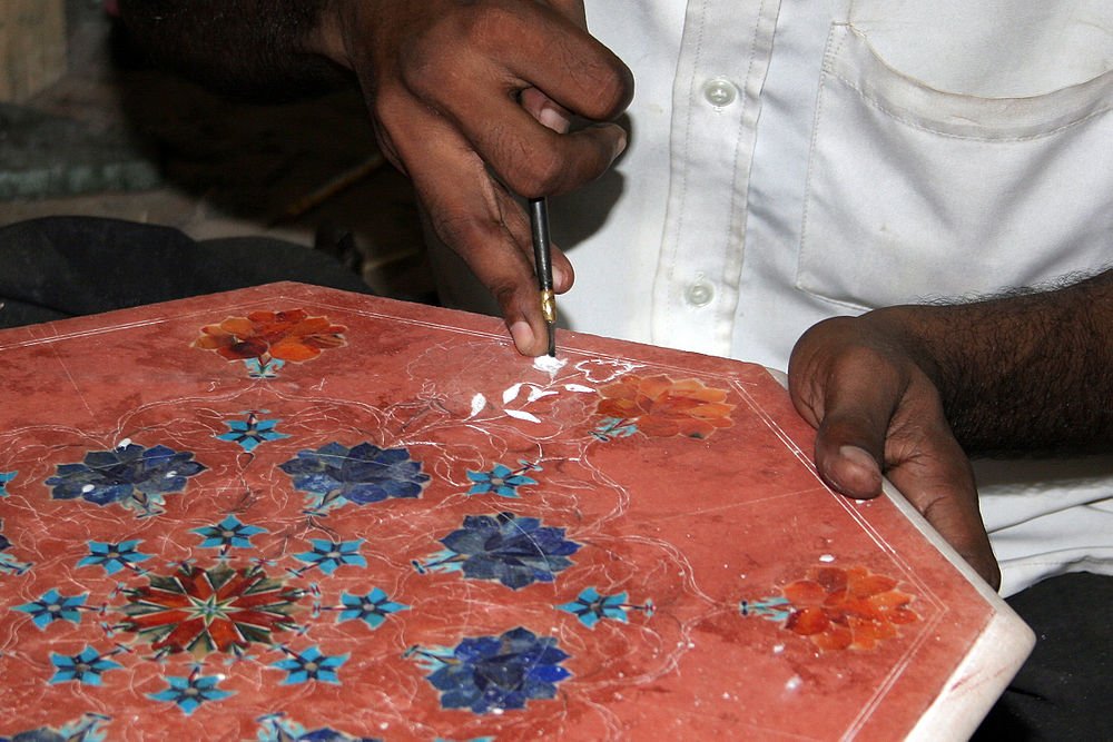 Artisan inlaying floral designs on red marble Craftsman hand inlaying floral patterns on red marble surface using traditional tools for decorative art
