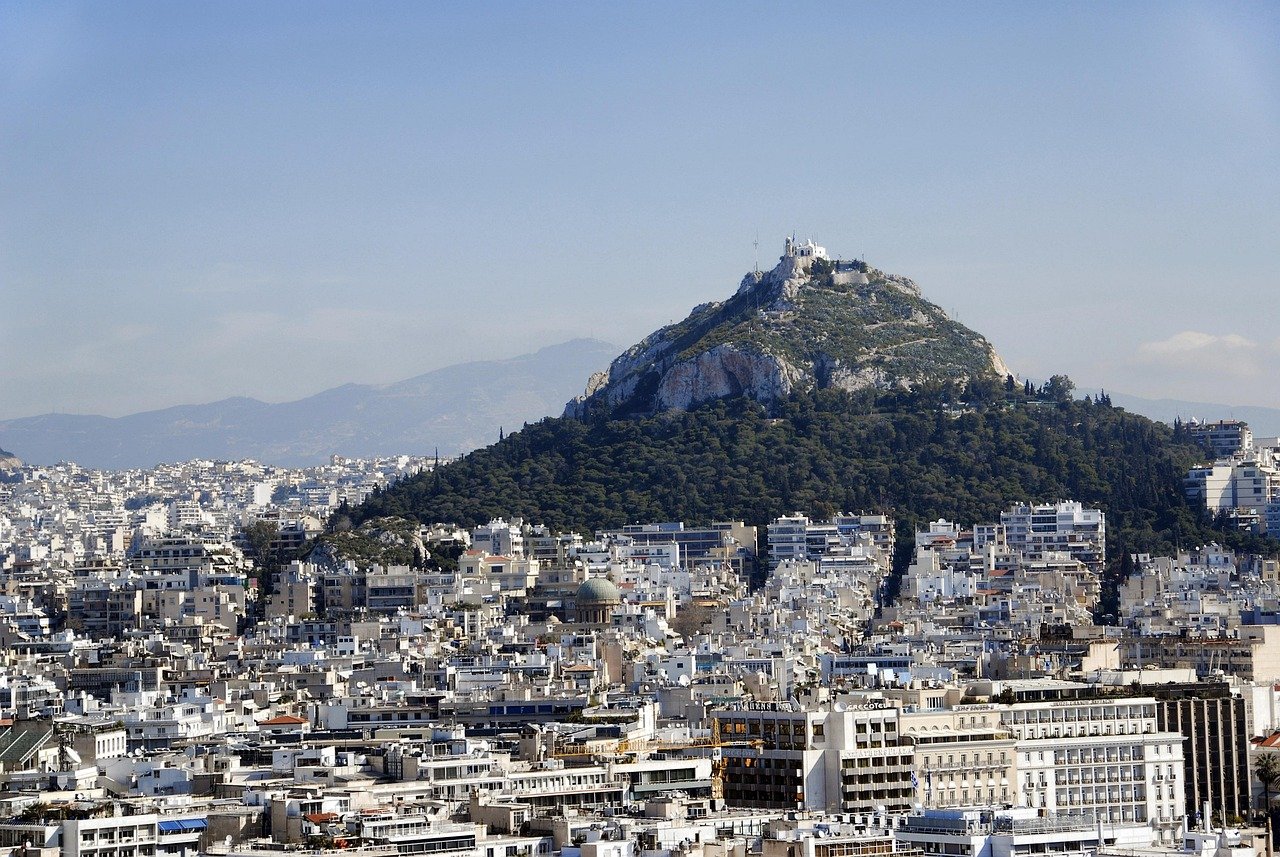 Panoramic view of Athens cityscape with Mount Lycabettus covered in greenery and buildings under clear blue sky