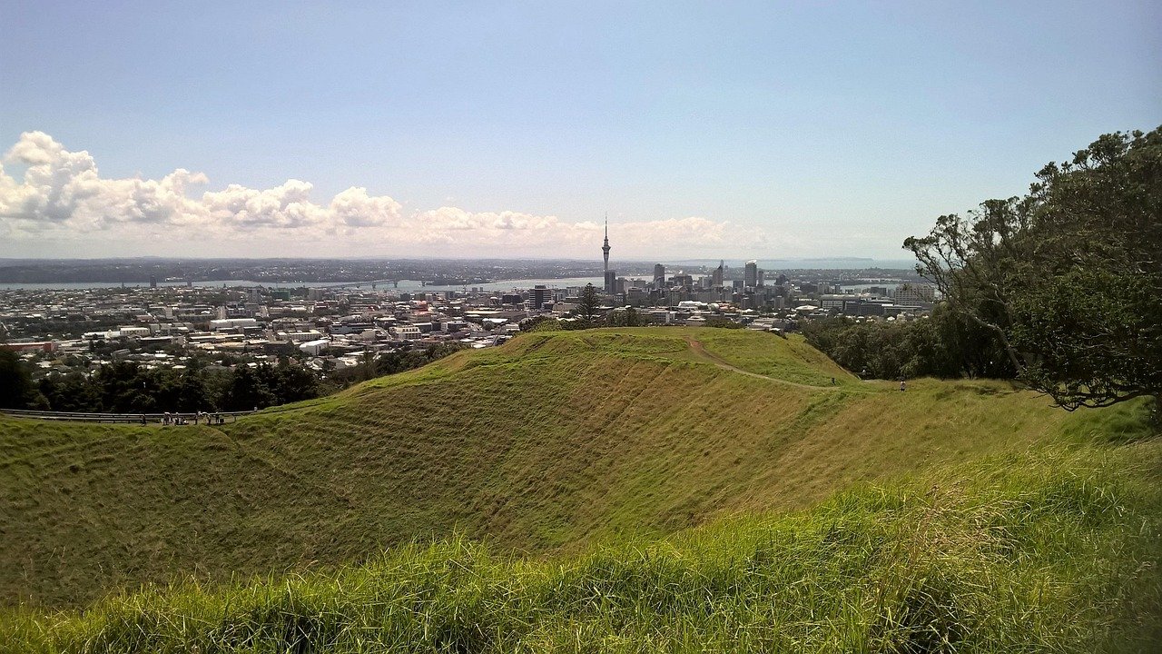 A panoramic view of Auckland city skyline with Sky Tower from a grassy volcanic crater on a clear sunny day
