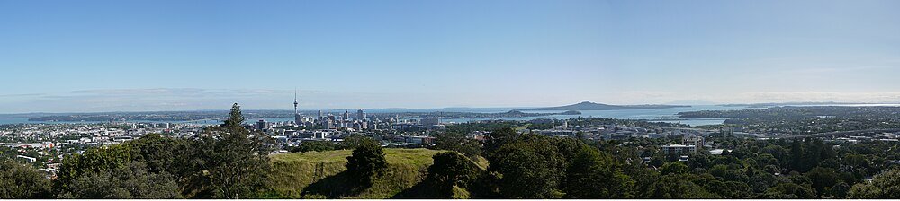 Auckland city skyline with Sky Tower and greenery Panoramic view of Auckland city skyline with Sky Tower, lush greenery, and surrounding water bodies under clear blue sky