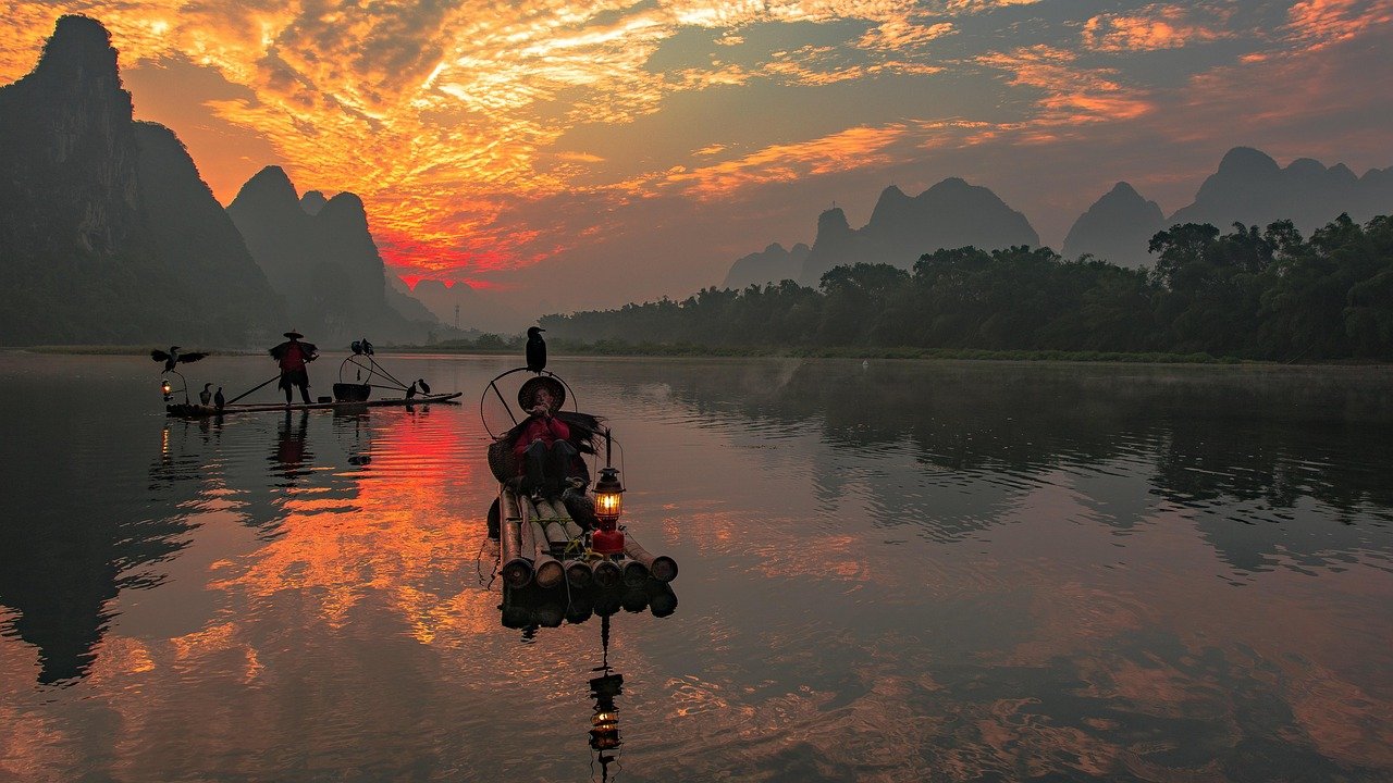 Traditional bamboo fishing boats on a calm river at sunset with dramatic orange sky and mountainous landscape