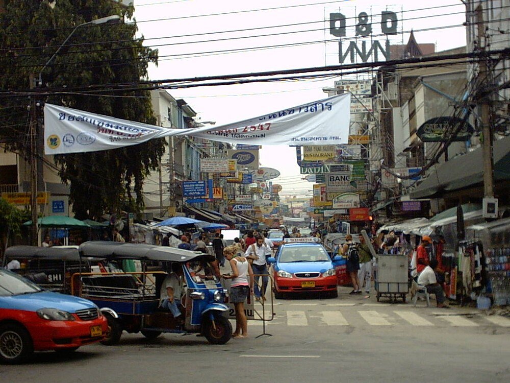 Busy Bangkok street with taxis and tuk-tuks Busy street in Bangkok with colorful taxis, tuk-tuks, pedestrians, and numerous shop signs in Thai language