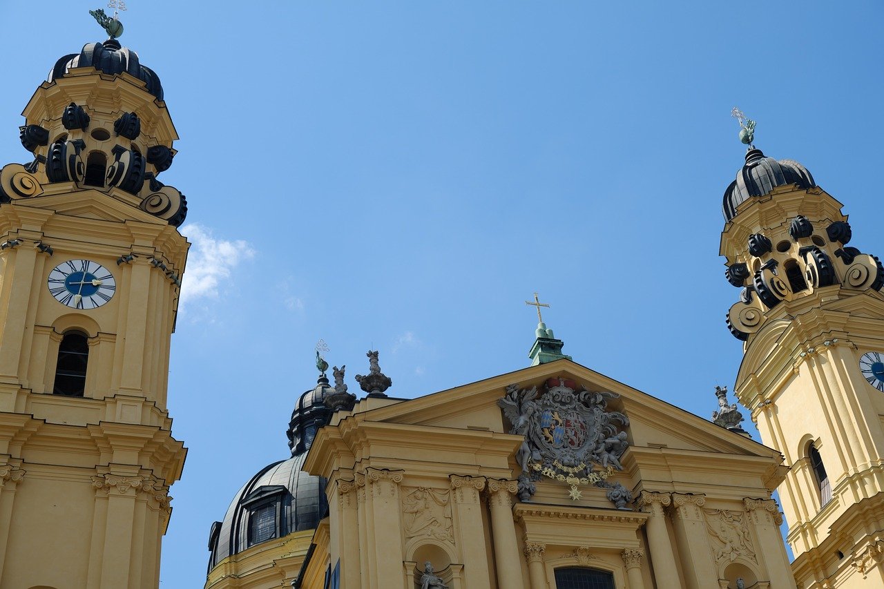 Baroque style yellow church towers with clocks and ornate details under clear blue sky