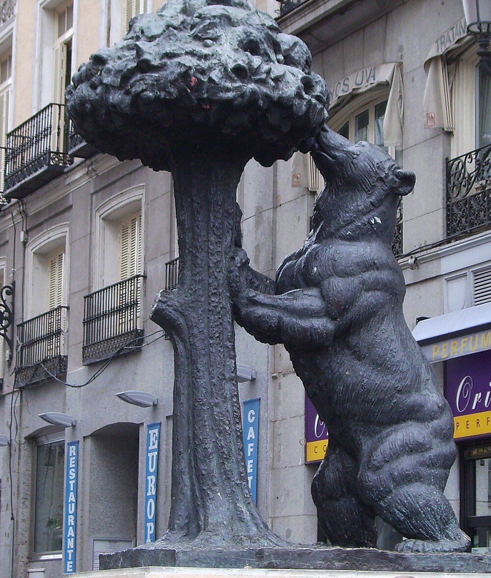 Bear statue reaching tree in city street Statue of a bear reaching up to a tree in an urban setting with buildings and balconies in the background