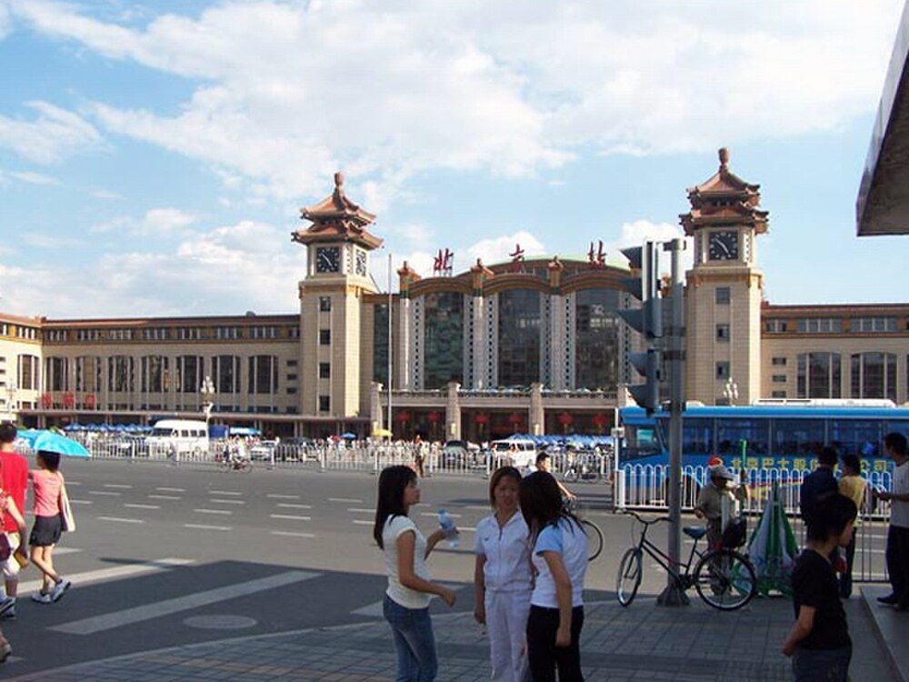 Beijing Railway Station exterior with people and buses Beijing Railway Station with people, buses, and bicycles on a sunny day in China