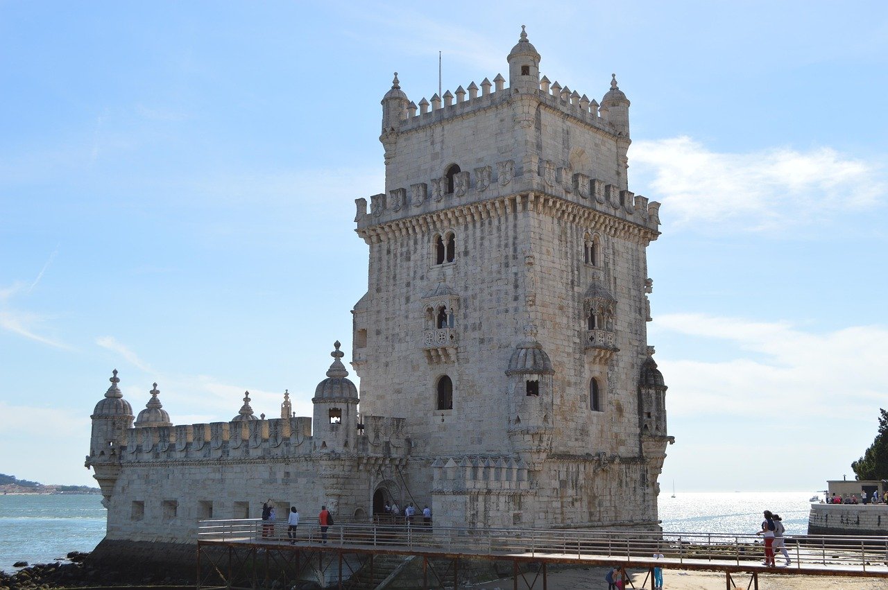 Historic Belem Tower in Lisbon Portugal on a sunny day by the Tagus River with tourists walking nearby