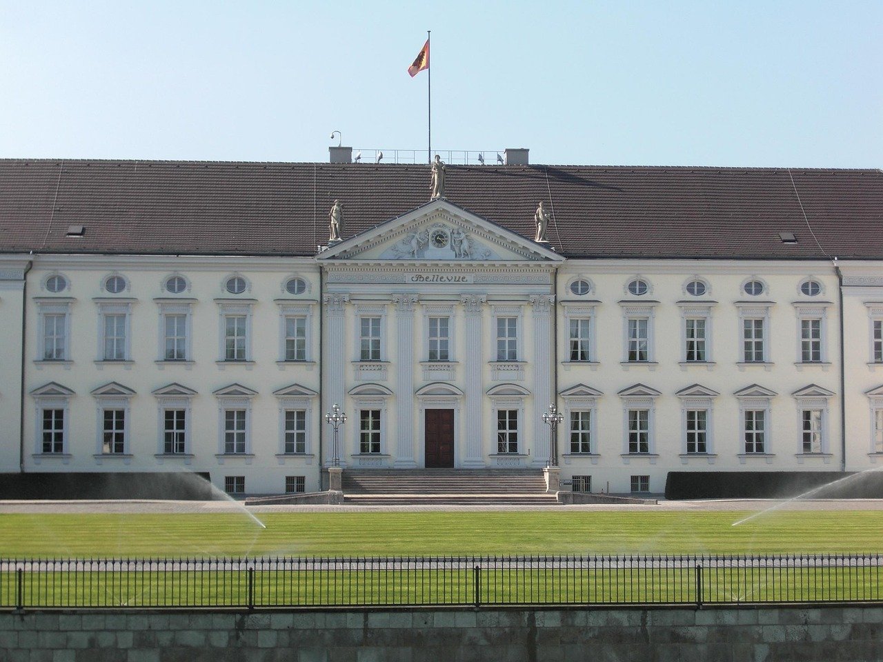 Bellevue Palace in Berlin with German flag, historic architecture, and well-maintained green lawn in front