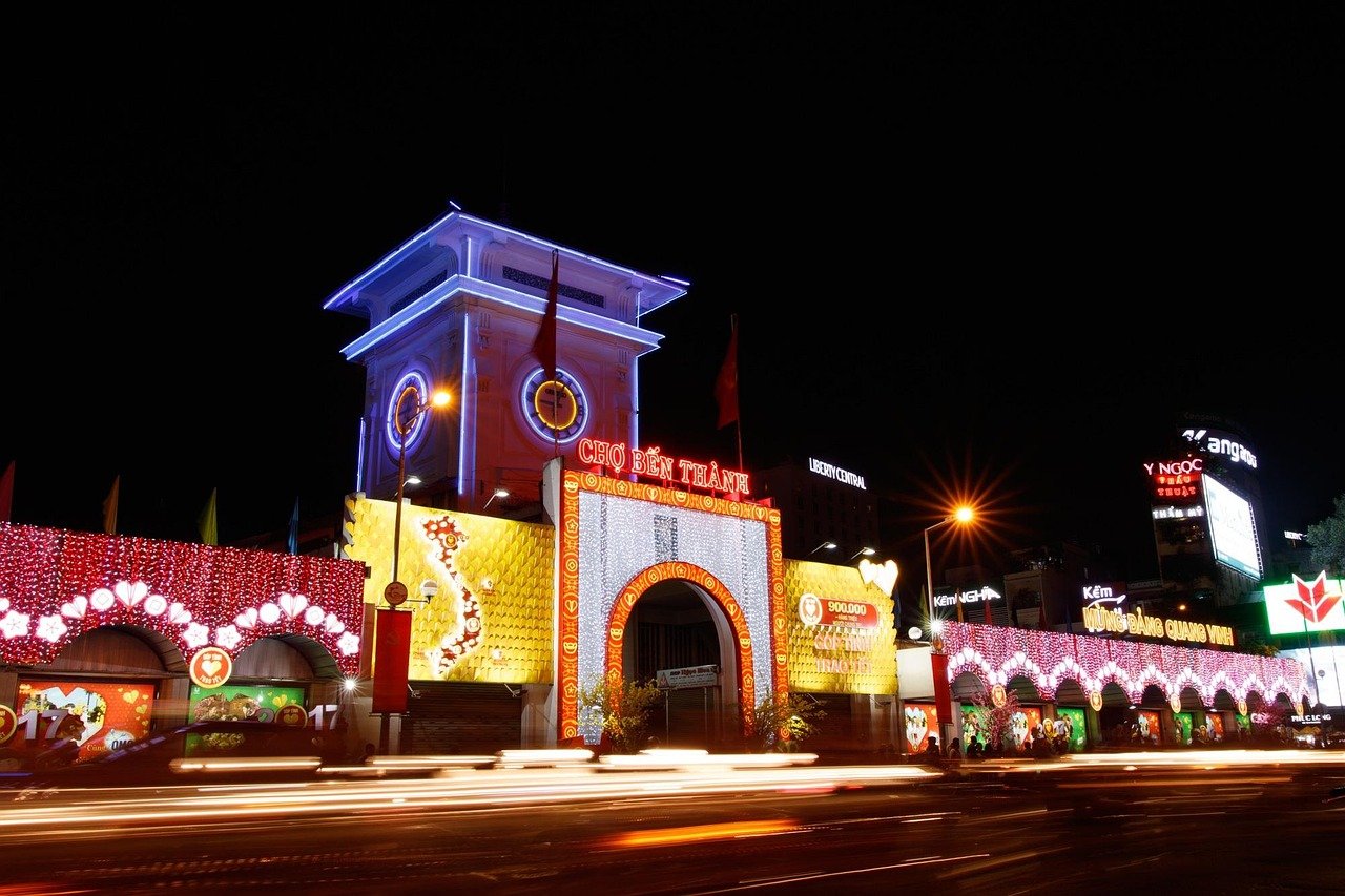 Night view of Ben Thanh Market in Ho Chi Minh City with vibrant neon lights and busy street traffic