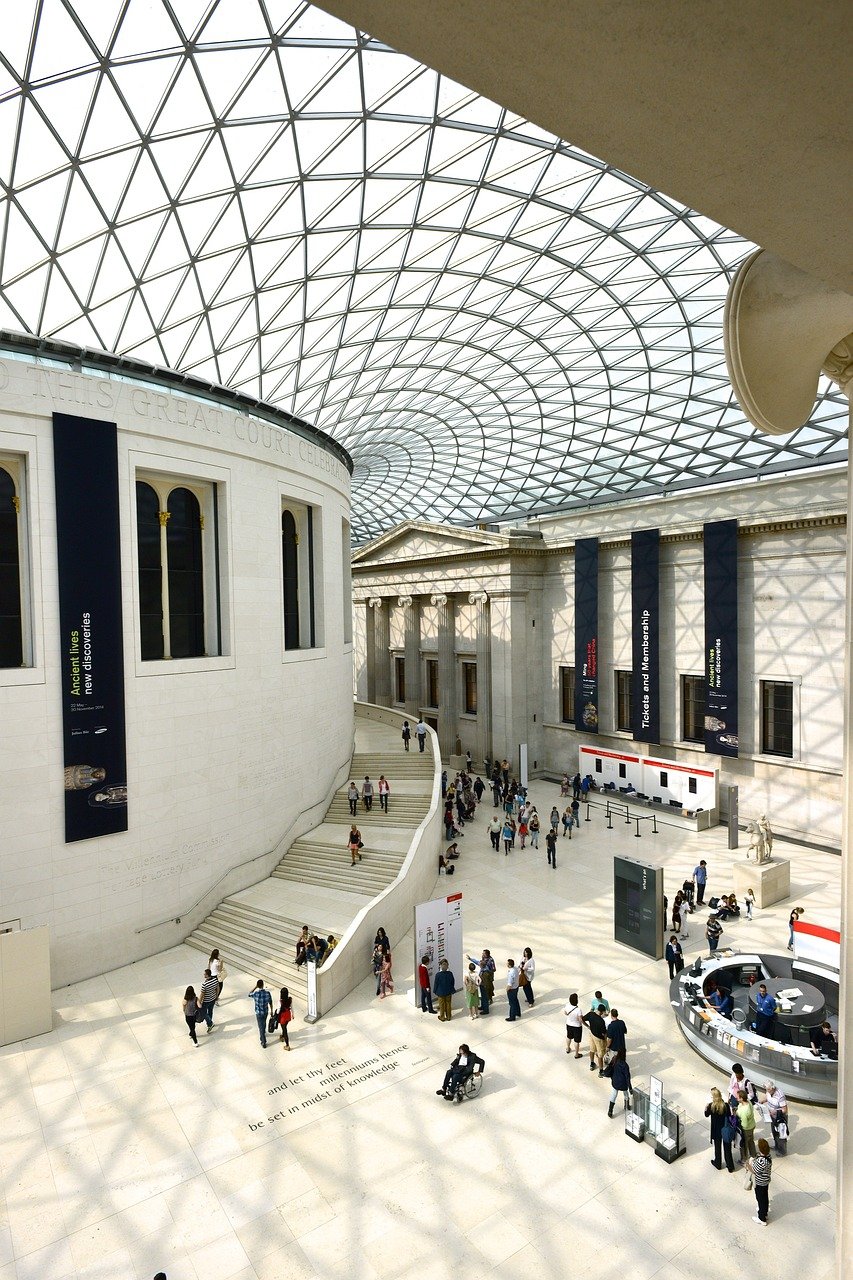 Interior view of the British Museum Great Court with glass roof and visitors exploring exhibits and information desks