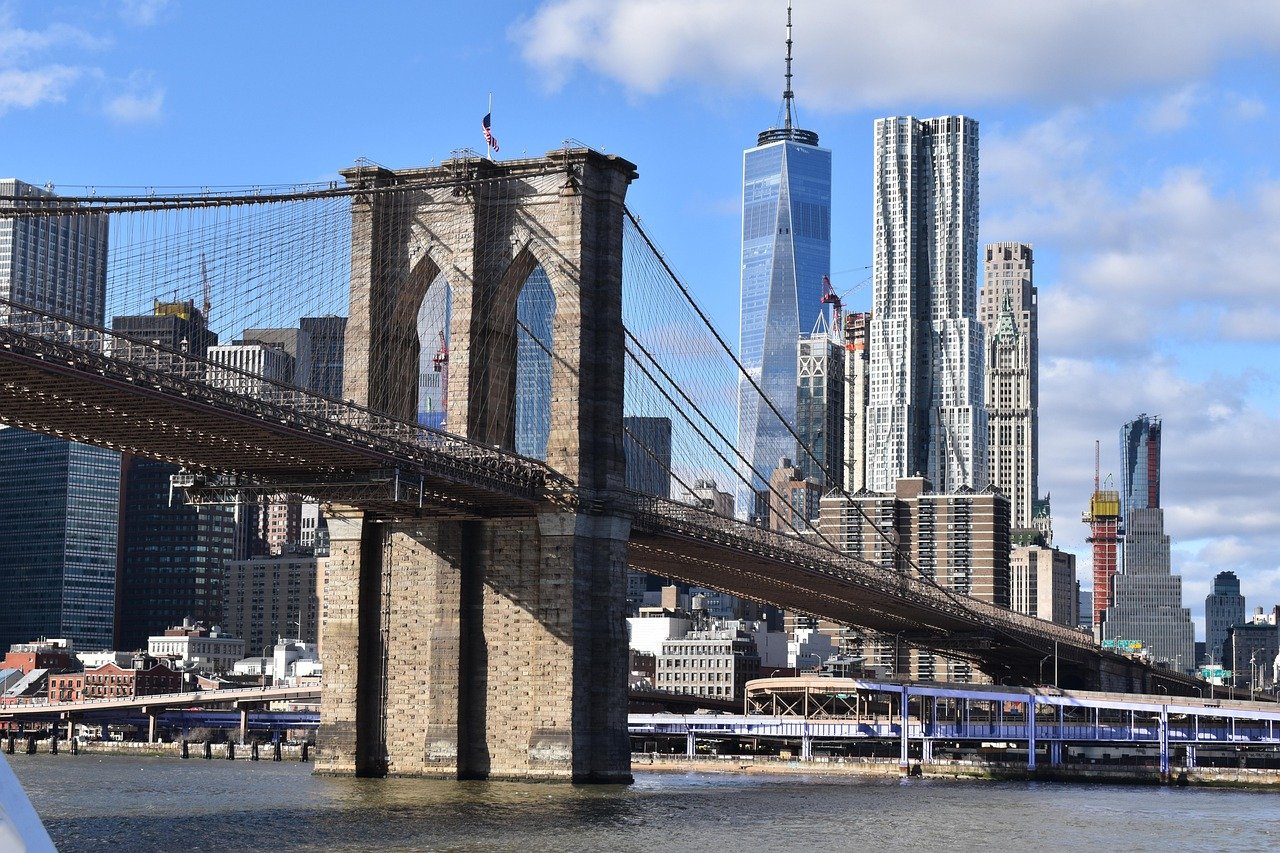 Brooklyn Bridge spanning East River with Manhattan skyline and One World Trade Center in background on a clear day