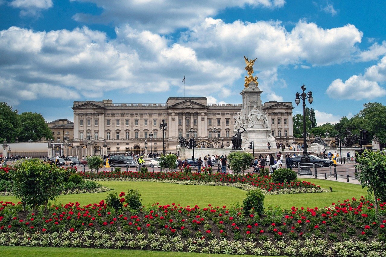 Buckingham Palace in London with Victoria Memorial and vibrant flower garden under a partly cloudy sky