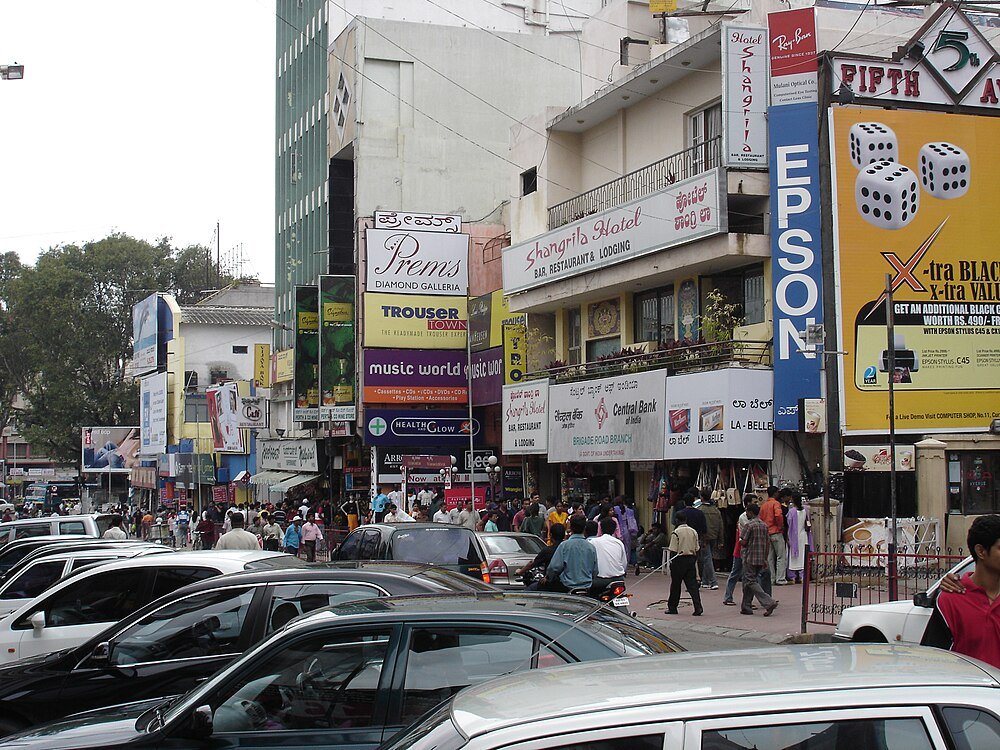 Busy urban street with shops and parked cars Busy street scene with shops, parked cars, and pedestrians in an urban area featuring signs for Epson, Central Bank, and Shangrila Hotel