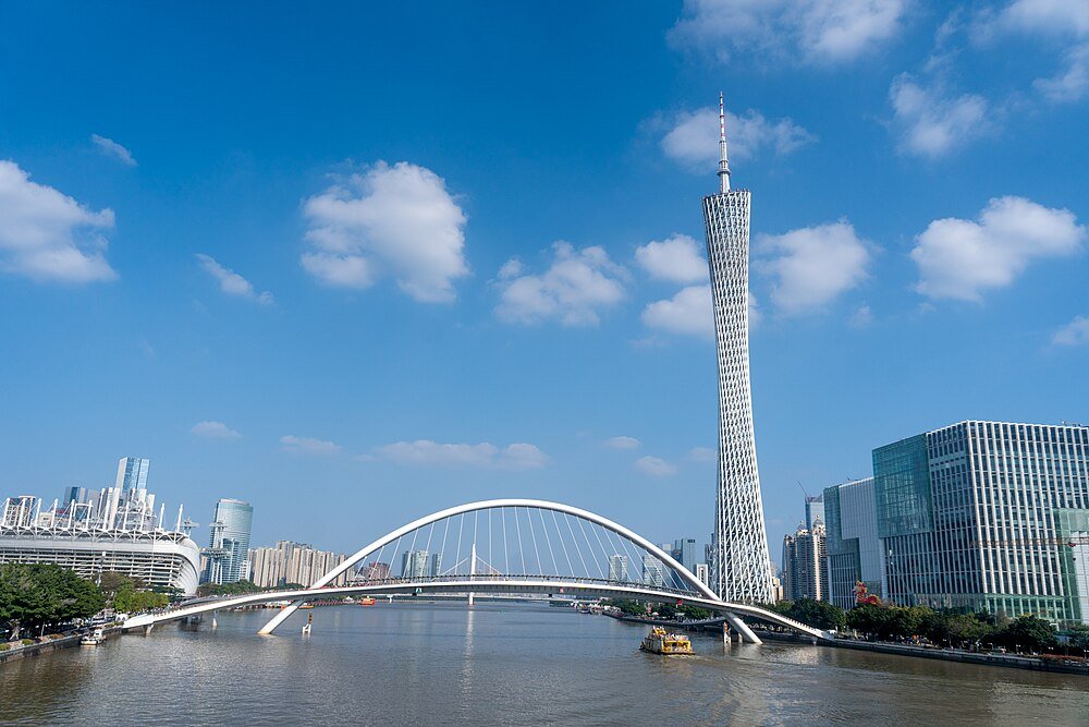 Modern cityscape with Canton Tower, a white arch bridge over the river, and high-rise buildings under a clear blue sky