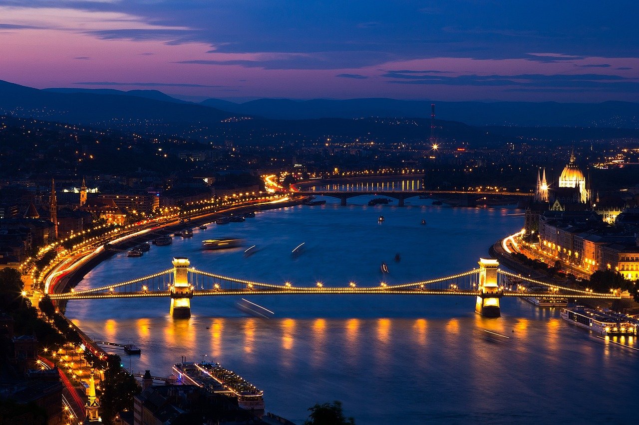 Night view of illuminated Chain Bridge over the Danube River in Budapest with city lights and hills in the background