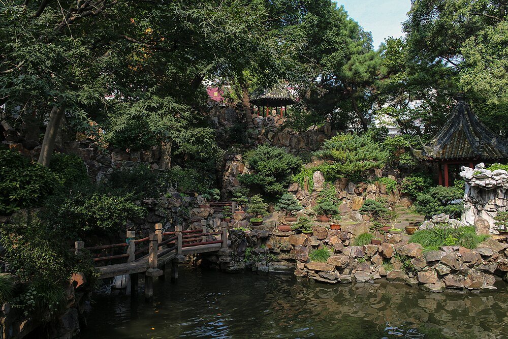 Traditional Chinese garden with stone bridge and pond Traditional Chinese garden with stone bridge, lush greenery, bonsai trees, and a serene pond reflecting natural surroundings