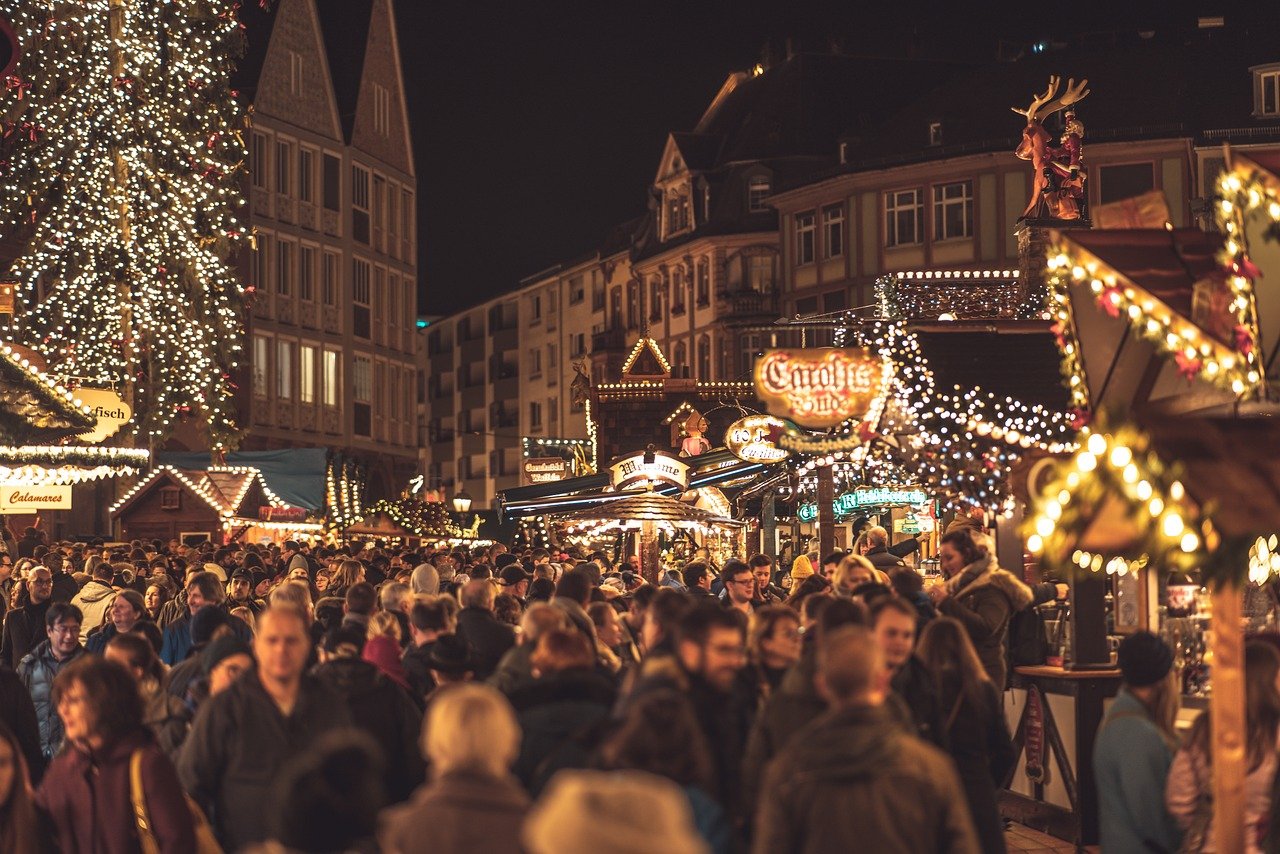 Crowded Christmas market at night with festive lights, decorated stalls, and people enjoying holiday shopping and celebrations