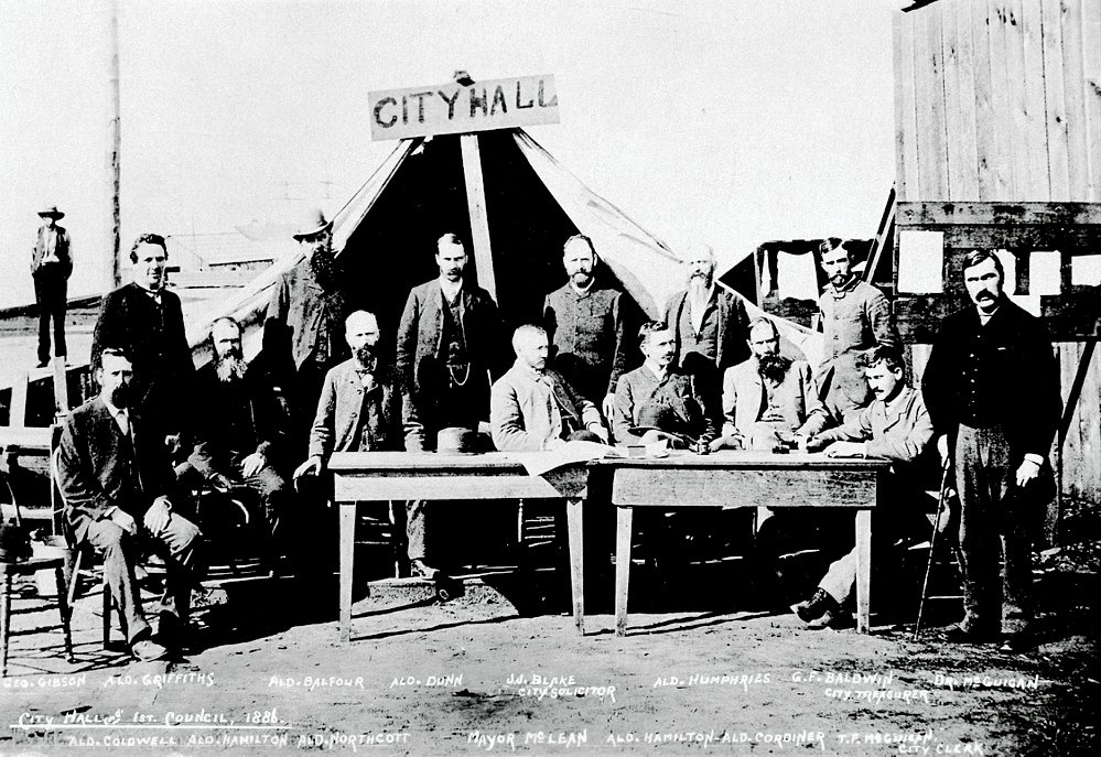 City Hall's First Council Meeting 1886 Historic black and white photo of City Hall's first council in 1886 with men in suits and a tent labeled City Hall