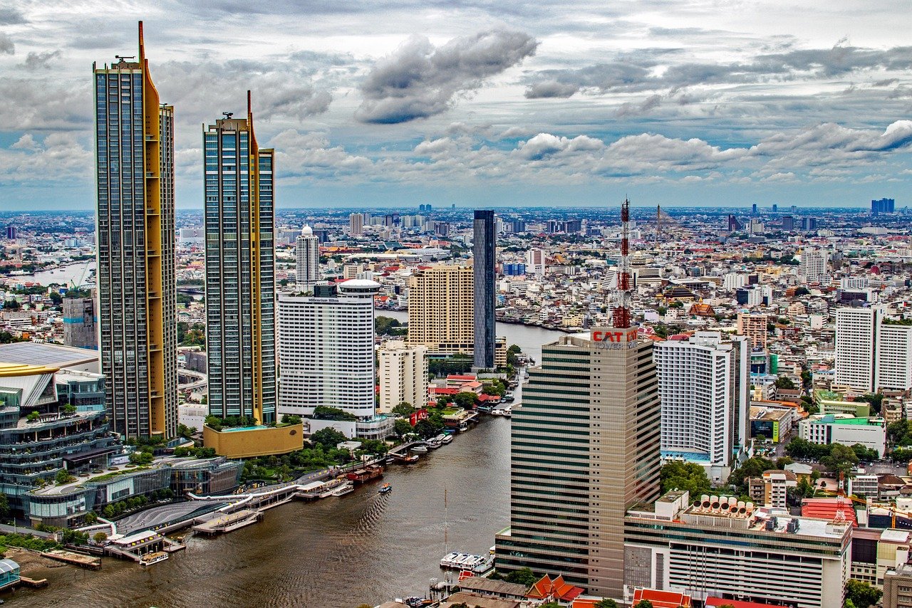 Aerial view of a modern city skyline with tall skyscrapers and a river running through the urban area under a cloudy sky