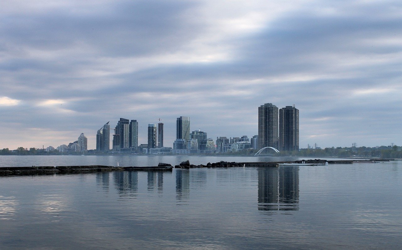 City skyline with modern high-rise buildings reflected on calm water under cloudy sky