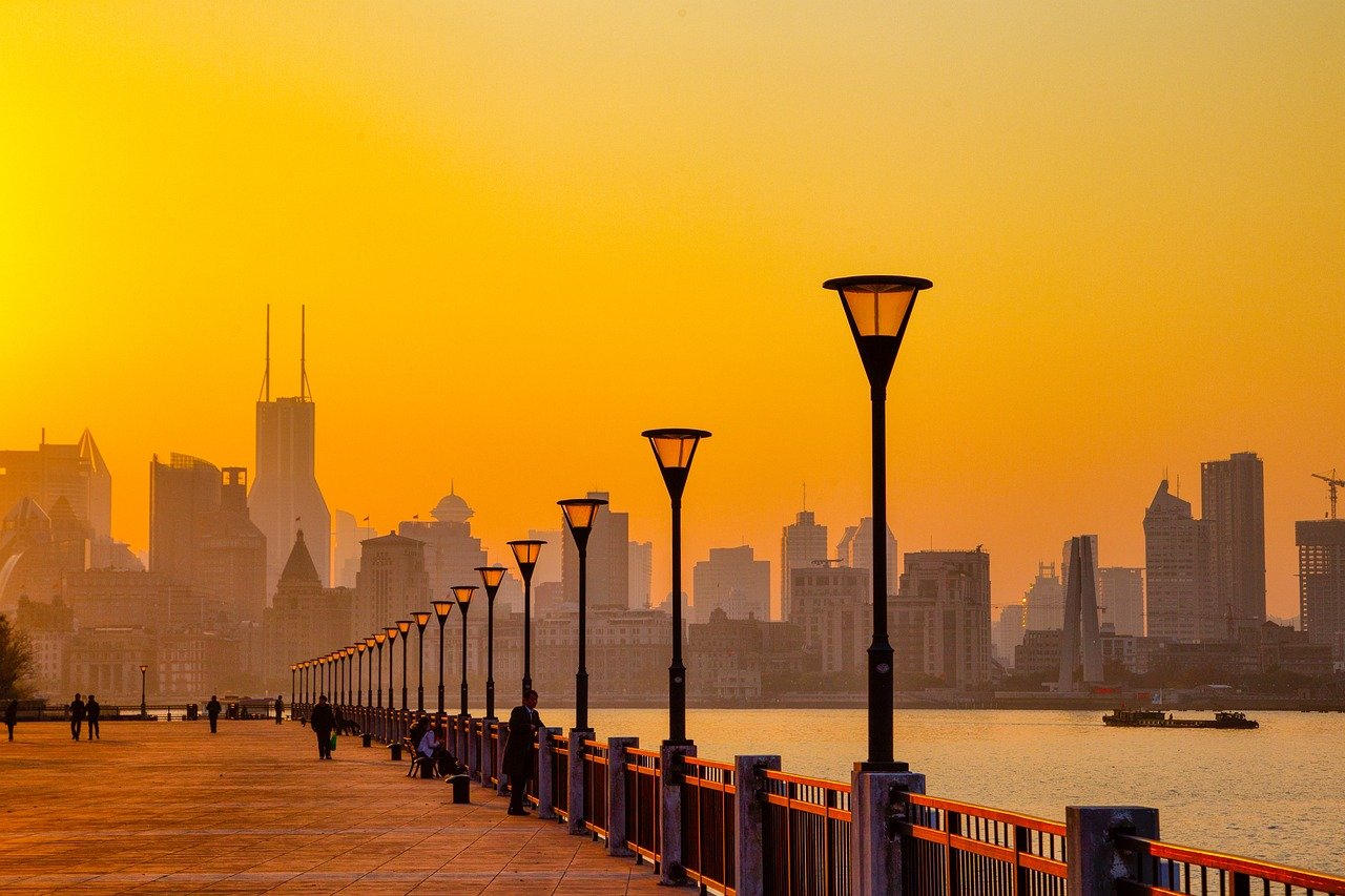 Sunset view of a city skyline with modern buildings and a waterfront promenade lined with street lamps