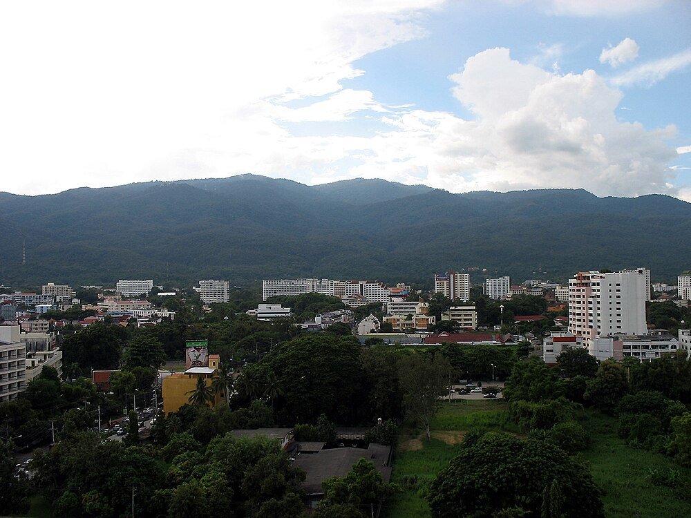 City skyline with mountains and greenery Cityscape with modern buildings and lush greenery under a partly cloudy sky and mountain range in the background
