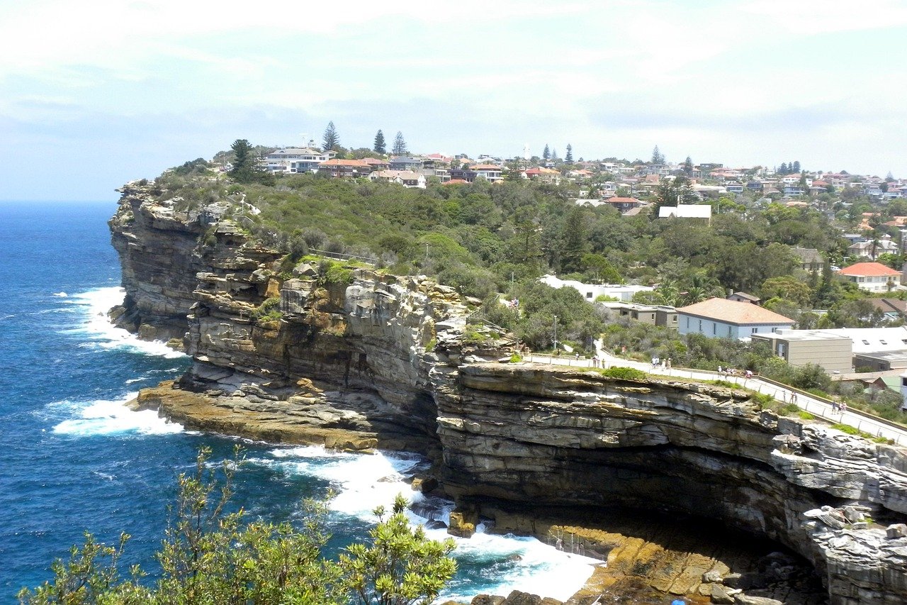 Scenic coastal cliff with ocean waves and residential houses on top, popular tourist spot with walking paths and greenery