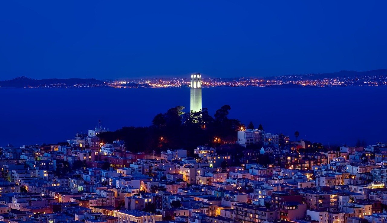Night view of Coit Tower illuminated on Telegraph Hill overlooking San Francisco cityscape and bay with distant lights
