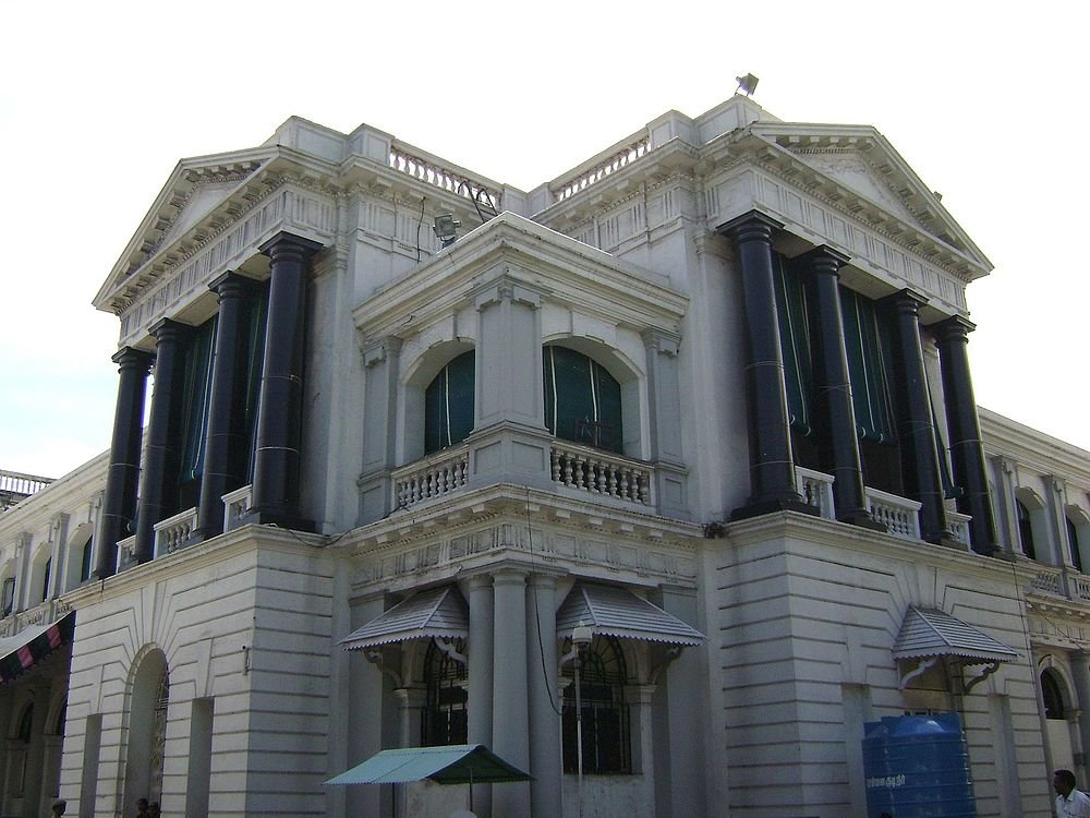 Historic colonial-era white building with large black columns and classical architectural details under bright sky