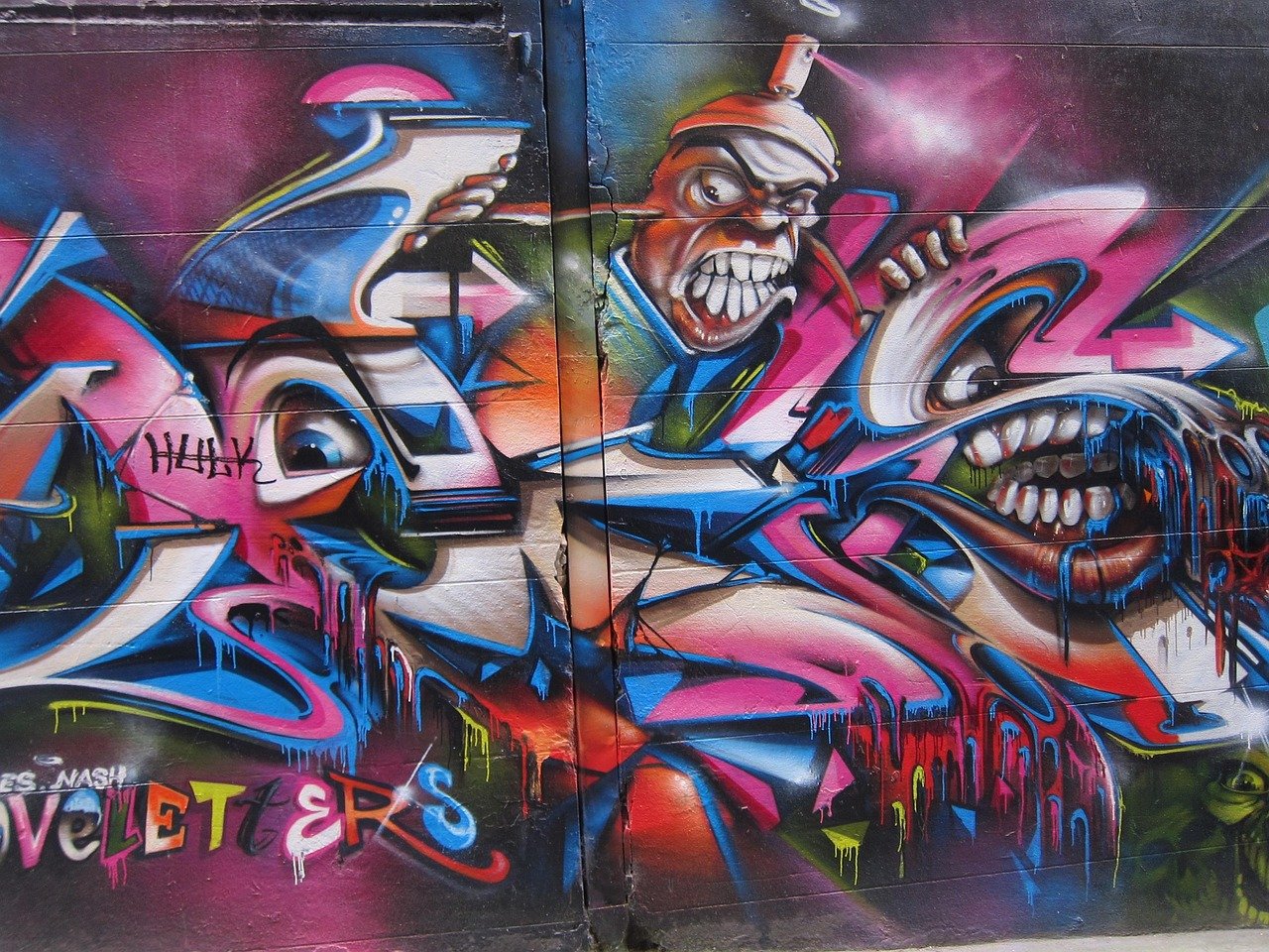Colorful graffiti art on wall featuring abstract faces with exaggerated teeth and vibrant dripping paint effects