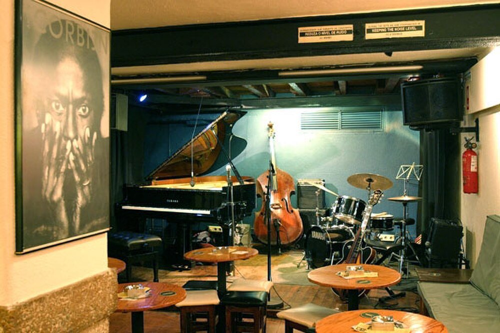 Jazz club stage with instruments and seating Cozy jazz club stage with piano, double bass, drum set, and small round tables with chairs in warm lighting