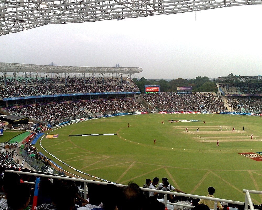 Cricket stadium filled with spectators during a live cricket match on a cloudy day