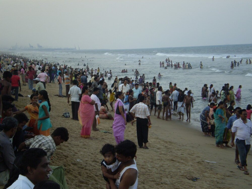 Crowded beach with many people enjoying the sea and sand, wearing colorful traditional and casual clothing in warm weather