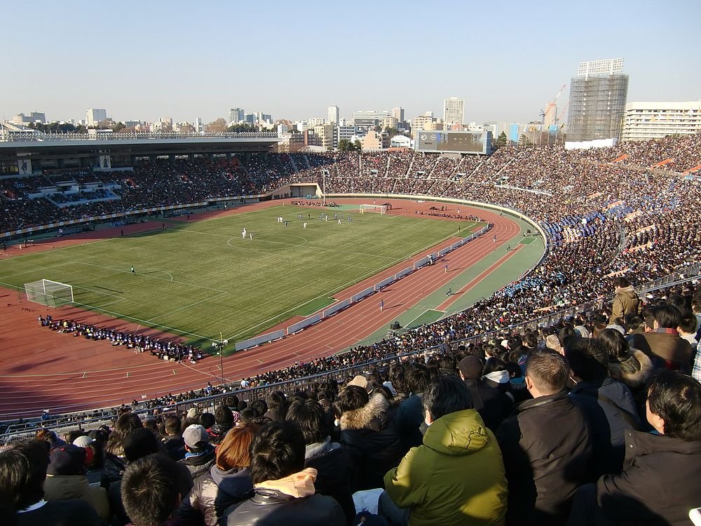 Crowded soccer stadium with fans watching a daytime football match on a sunny day in an urban area