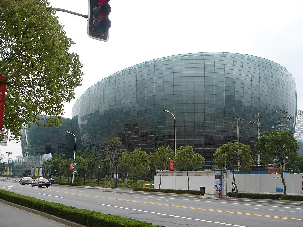 Modern glass building with curved design near a street with trees and cars under a traffic light