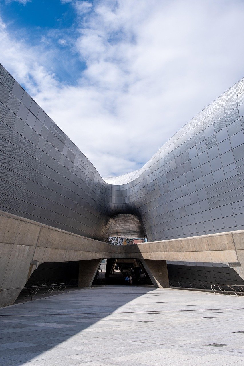 Modern architectural structure with curved metallic panels and concrete base under a partly cloudy sky