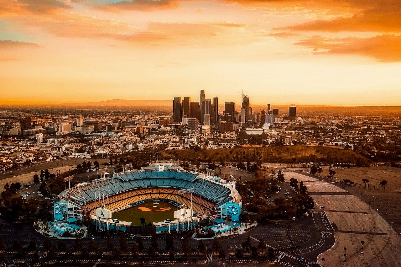 Aerial view of Dodger Stadium with Los Angeles city skyline at sunset, showcasing baseball field and urban landscape.